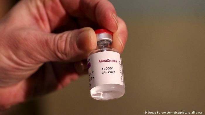 A hand holds up a container of AstraZeneca vaccine