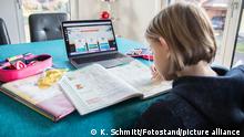 Bamberg, Deutschland 31. Dezember 2020: Auf einem Wohnzimmertisch steht ein Laptop an dem gerade ein Kind arbeitet, daneben liegen verschiedene Schulutensilien und ein aufgeschlagenes Buch mit einem Mundschutz.