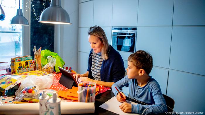 Mother with ipad and child with pen and paper sitting at a cluttered desk