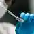 nurse in protective gear drawing the vaccine into a syringe