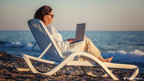 Foto simbólica de una persona sentada en la playa que trabaja con una laptop.