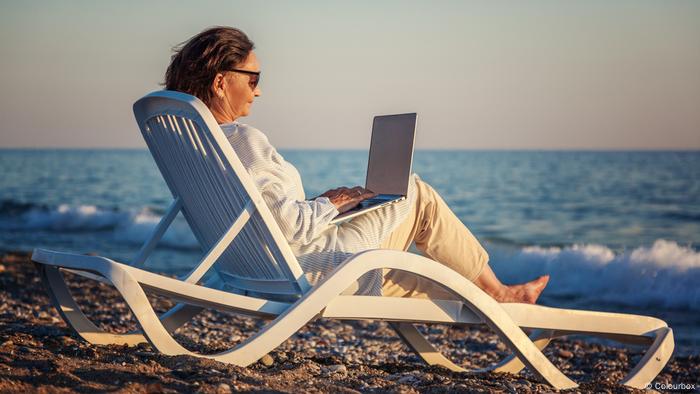 Foto simbólica de una persona sentada en la playa que trabaja con una laptop.
