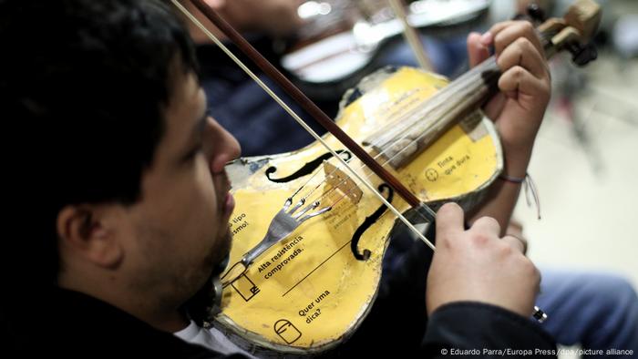 Hombre tocando un violín fabricado con material reciclado.