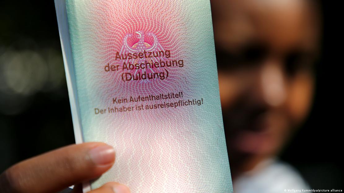 Një grua e sfumuar në sfond duke mbajtur në dorë dokumentin e lëshuar nga qeveria gjermane që shkruan Duldung: 