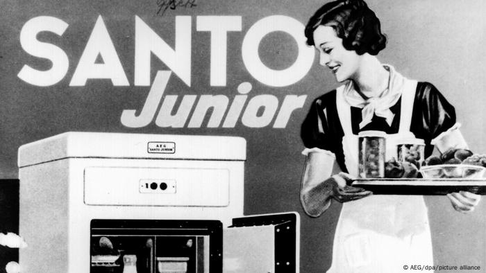 Frau mit Tablett steht vor einem Kühlschrank auf einem Werbeplakat für den ersten elektrischen Kühlschrank von AEG um 1935