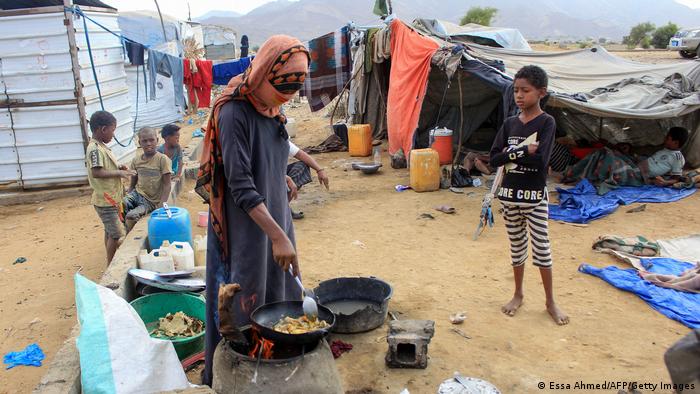 Yemeni children play near tents as a woman cooks outdoors at a makeshift camp for the displaced who fled fighting between Houthi rebels and the Saudi-backed government,