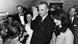 Der US-amerikanische Vizepräsident Lyndon B. Johnson steht mit erhobener Hand neben Jacqueline Kennedy, umringt von mehreren Leuten Der US-amerikanische Vizepräsident Lyndon B. Johnson steht mit erhobener Hand neben Jacqueline Kennedy, umringt von mehreren Leuten