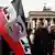 QAnon-Anhänger vor dem Brandenburger Tor in Berlin. Im Vordergrund eine Reichskriegsfahne: darauf ein Foto von Donald Trump, daneben ein großes "Q" und der Schriftzug WWG1WGA