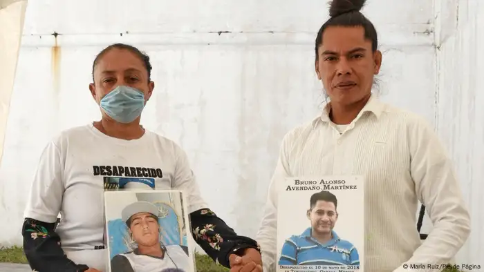 Performance artist Lukas Avendaño and friend hold photos of their loved ones they are still searching for.