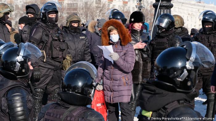 A woman wearing a purple coat and fur hood is surrounded by riot police during an unauthorized rally