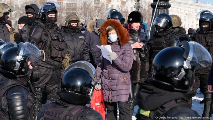 A woman wearing a purple coat and fur hood is surrounded by riot police during an unauthorized rally