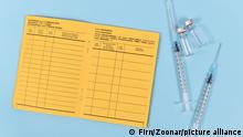 Vaccine concept with syringes, vials and empty yellow international certificate of vaccination with German and English text on blue background / Europäischer Impfausweis mit Spritzen