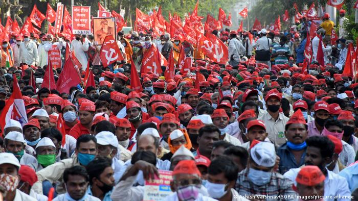 Indische Bauern demonstrieren auf einer Straße in Mumbai mit roten Hüten und roten Flaggen, auf denen Hammer und Sichel zu sehen sind