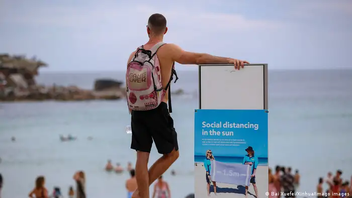 A man stands beside a social distancing notice board at Bondi beach in Sydney, Australia