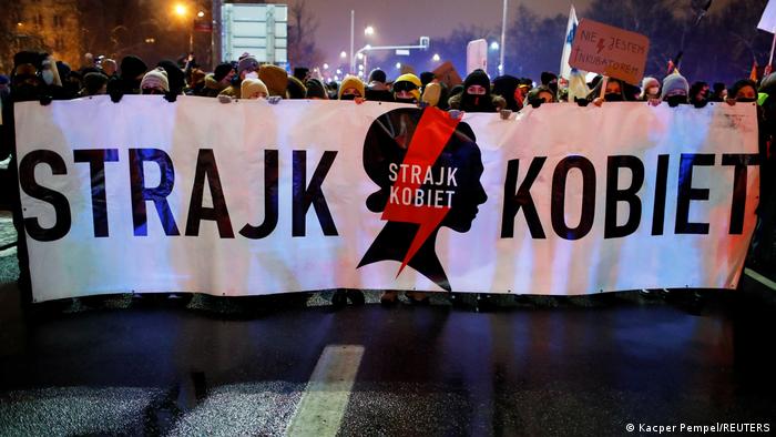 Proteste gegen das Urteil zur Einschränkung des Abtreibungsrechts in Warschau, Polen, am 28. Januar 2021: Demonstrierende tragen eine Banner mit der Aufschrift Strajk Kobiet (Frauenstreik), dahinter zeigt ein Demonstrant ein Plakat mit der Aufschrift Ich bin kein Brutkasten