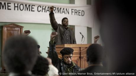 Eine Szene aus dem Film Judas and the Black Messiah zeigt einen Schwarzen, der mit gereckter Faust hinter einem Rednerpult steht. 