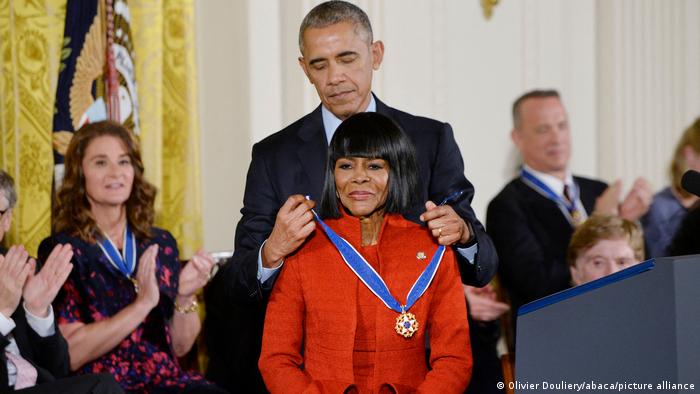 Barack Obama places a band with a medal around Cicely Tyson's neck, people look on and applaud 