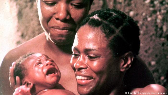 In a still from Roots, Cicely Tyson holds a baby and Maya Angelou stands next to her
