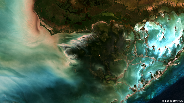 On the satellite image, blue, turquoise, white colors of the sea mix with green and brown colors of the coast.