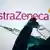 Hand in Handschuh hält Impfstoffampulle und Spritze vor dem Firmenlogo von AstraZeneca