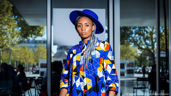  Wanuri Kahiu, woman wearing colorful shirt and a blue hat looks into camera 