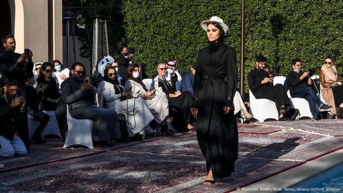 A model wears a white cowboy hat with a long-sleeved, ankle-length black dress on the catwalk.