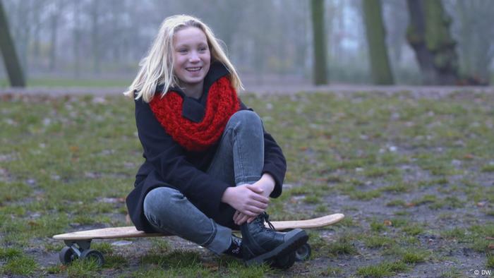 Helena Zengel is sitting in the forest on a skateboard, smiling. Helena Zengel is sitting in the forest on a skateboard, smiling.