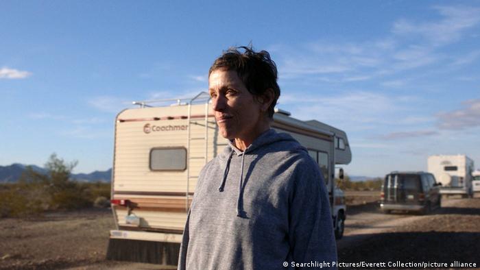A still from Nomadland with Frances McDormand in a vast landscape next to camper vans