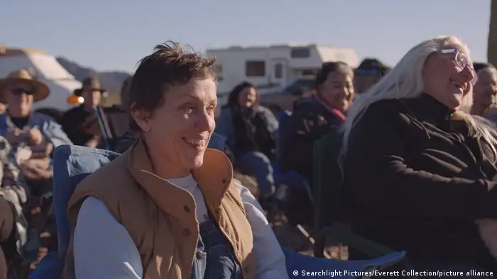 Frances McDormand in Nomadland, sitzend zwischen Menschen im Freien