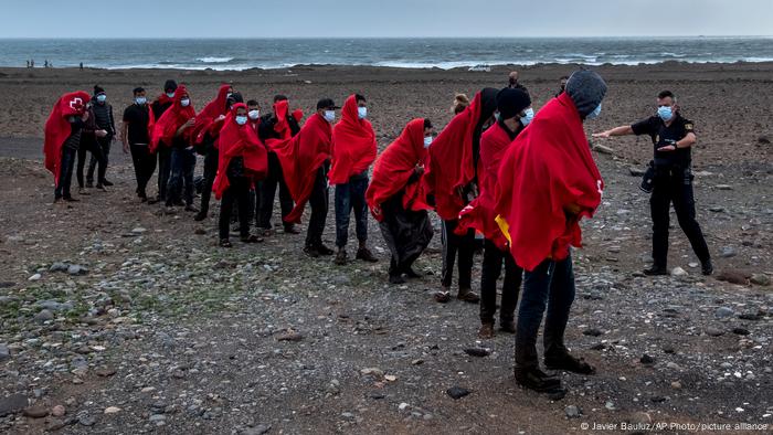 A number of migrants walk in line as Spanish officials look on.