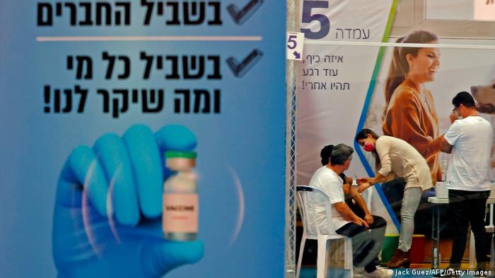 A sign in foreground as Israelis get the COVID-19 vaccine at a local vaccination center