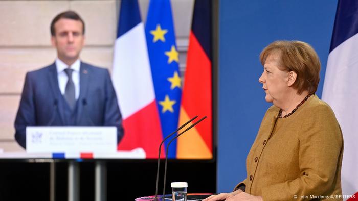 Chefe de governo alemã Angela Merkel, com presidente francês Emmanuel Macron ao fundo