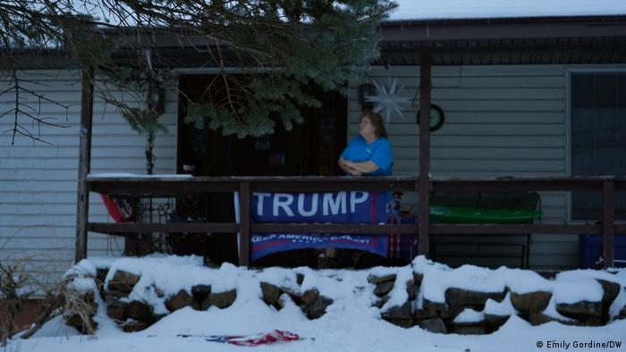 Moradora de Piketown em sua varanda, atrás de um cartaz de apoio a Trump