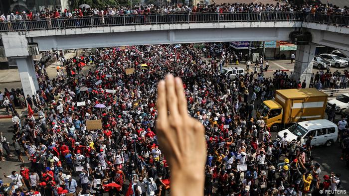 Hand showing the three-finger salute against the backdrop of a crowd of demonstrators