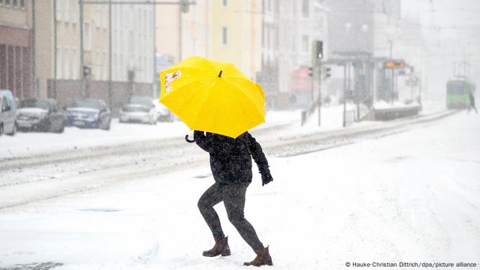Eine Frau mit Regenschirm überquert eine Straße in Hannover, Niedersachsen