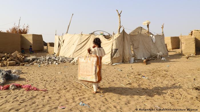 Mädchen geht mit einer großen Tasche auf eine aus Zeltplanen bestehende Notunterkunft zu
