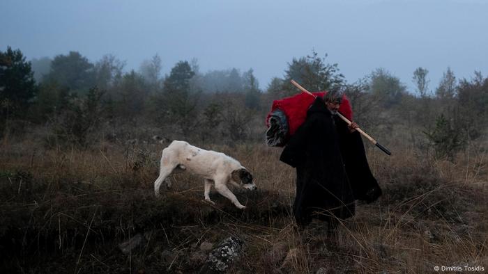 A shepherd walks in the morning fog carrying heavy blankets in Greece