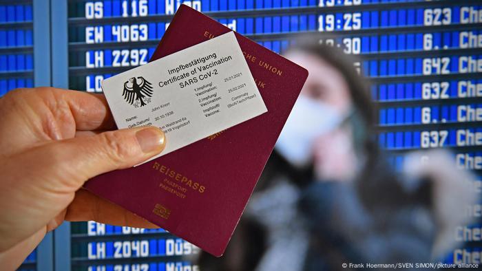 A hand holding a German passport and a certificate of a SARS CoV-2 vaccination