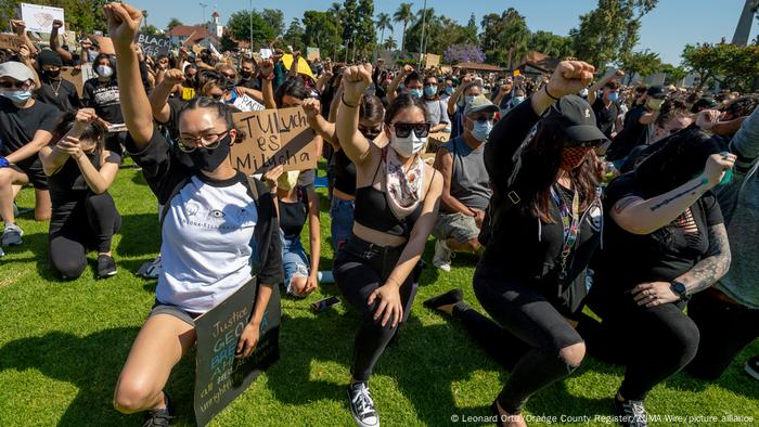 Demonstrators in the park kneeling down and holding their fists up in the air. 