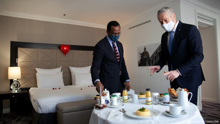 Two men stand near a breakfast table in a hotel room