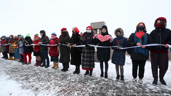 Na neve, mulheres com roupas de frio seguram um cordão branco, flores e corações de papel.