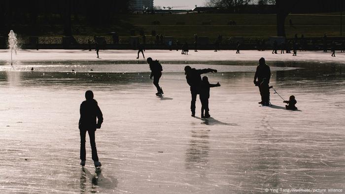 In einem teilweise zugefrorenen Teich in Köln laufen und fahren die Menschen Ski