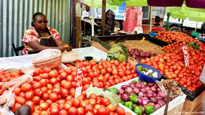 A lady selling tomatoes and other vegetables at a market stall