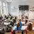Sala de aula cheia de crianças e a professora dando a aula com áscara na Alemanha