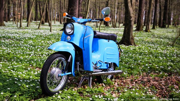 A blue moped parked in a forest.