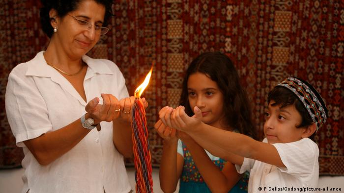 Zwei Kinder und eine Frau strecken ihre Hände einer Kerze entgegen.
