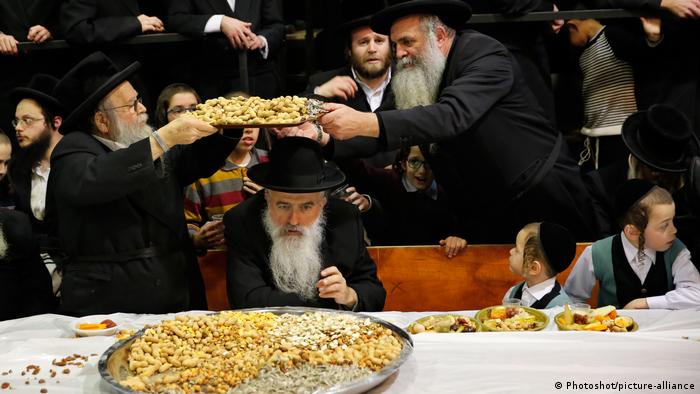 Orthodoxe Juden sitzen am Tisch, vor ihnen Platten mit Früchten 