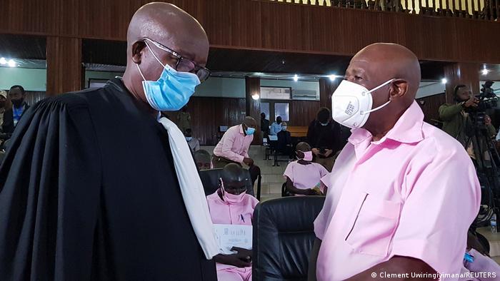 Paul Rusesabagina, dressed in a pink, standard-issue prison uniform and wearning a mask, speaks to his lawyer