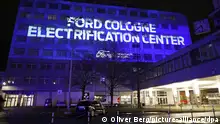 Ein Auto steht auf dem Werksgelände vor einem Gebäude auf das eine Lichtprojektion mit der Aufschrift Ford Cologne - Electrification Center geworfen wird. Der Automobilhersteller Ford will seinen weltweit ersten vollelektrischen Kleinwagen in Köln bauen.