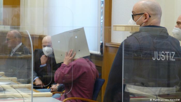 Eyad A. in court hiding his face behind a paper envelope